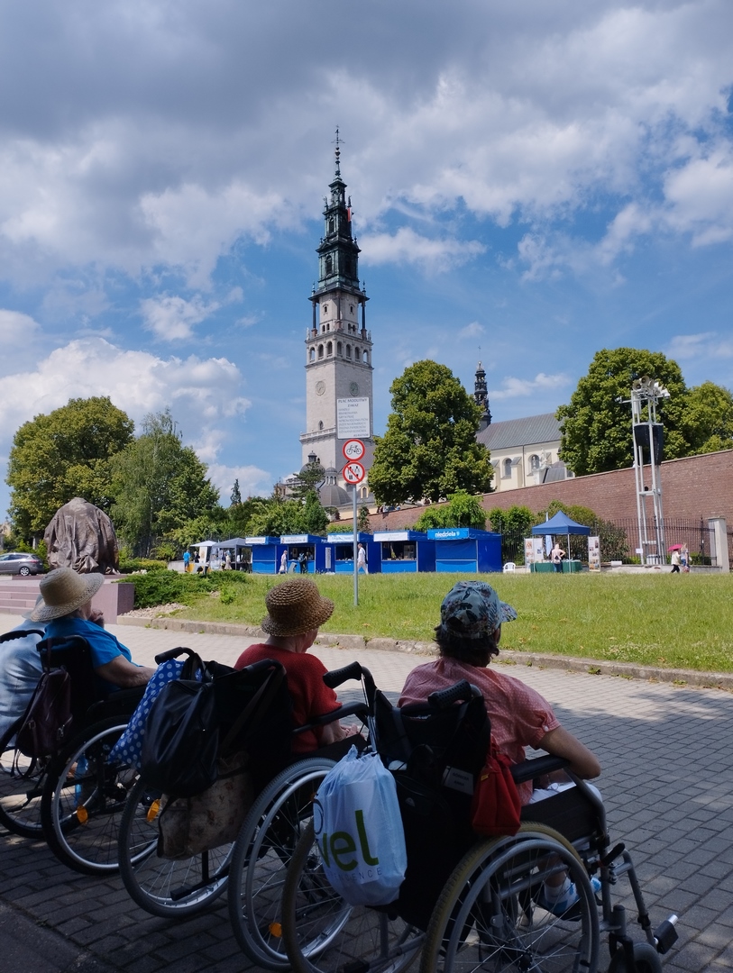 Trzy osoby siedzące na wózkach inwalidzkich spoglądające na Kościół.