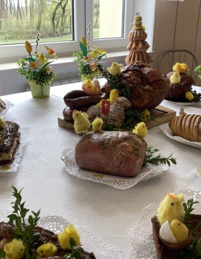 Wielkanocny stół przykryty białym obrusem a na nim poukładane pisklaki, pisanki, chleb, jaja i pisanki, babeczki, ciasta. Wszystko udekorowane żółtymi tulipanami.