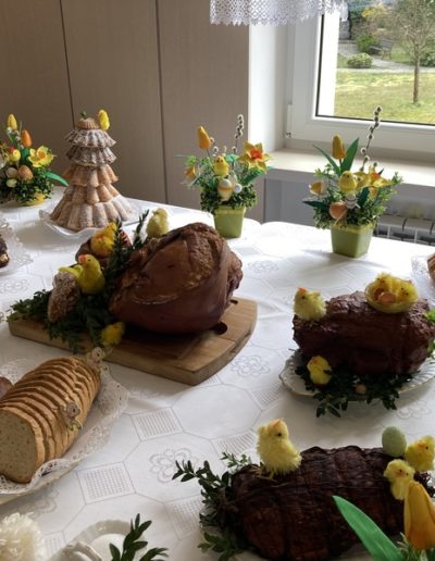 Wielkanocny stół przykryty białym obrusem a na nim poukładane pisklaki, pisanki, chleb, jaja i pisanki, babeczki, ciasta. Wszystko udekorowane żółtymi tulipanami.