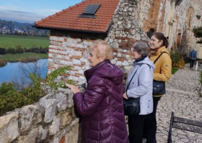 Grupa kobiet wpatrzona na rzekę, stoją na dziedzińcu.