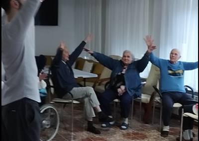 Mieszkańcy w sali siedzą z rozłożonymi rękoma i patrzą na animatora.