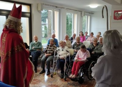 Zza pleców Świętego Mikołaja widać siedzących w sali mieszkańców
