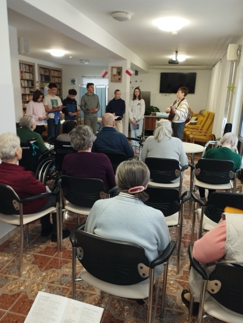 Grupa ludzi słucha kolędowania w sali